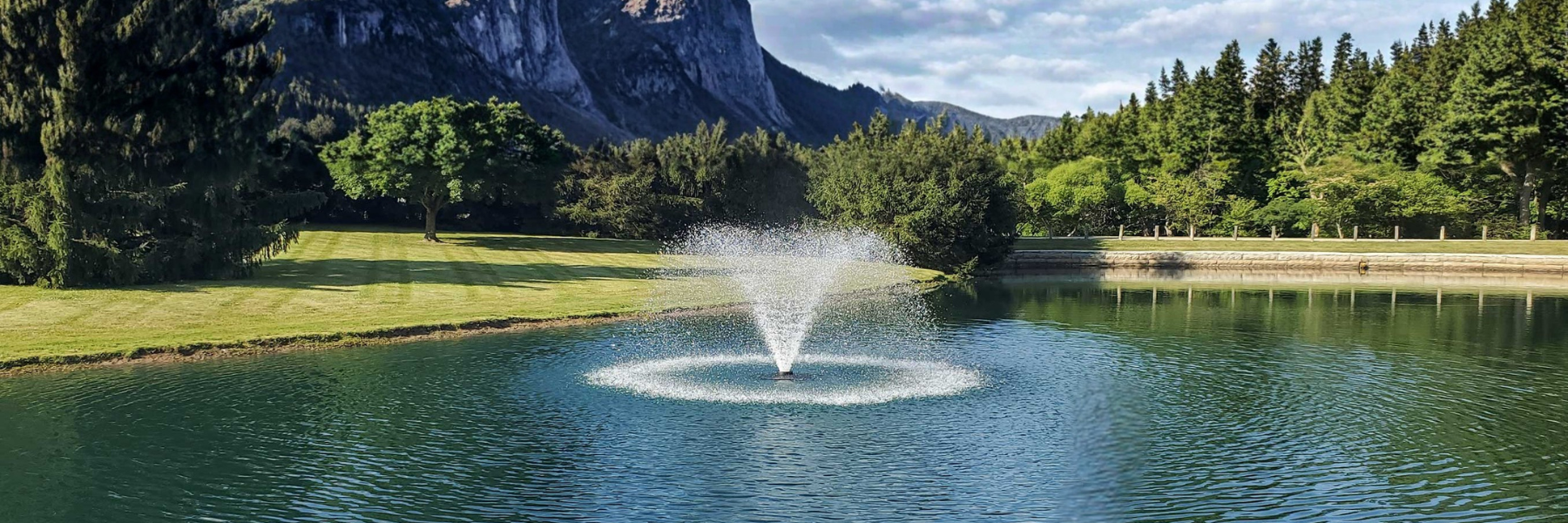 Aerating Pond Fountain in a pond at a golf course with mountains in the background - Benefits of Pond Aeration