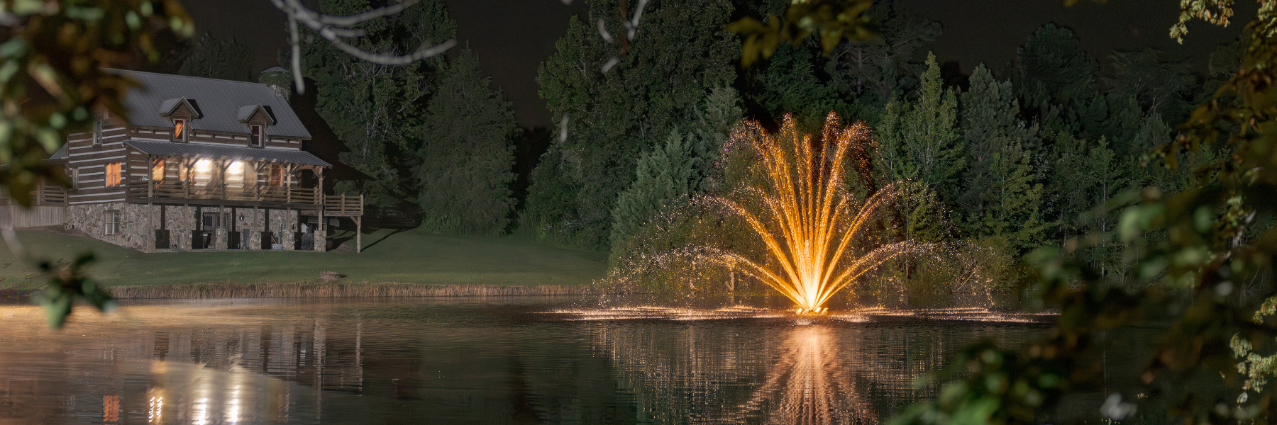 Fishing lodge with a fountain with lighting at night on a pond - Are Fountains Good for Ponds?