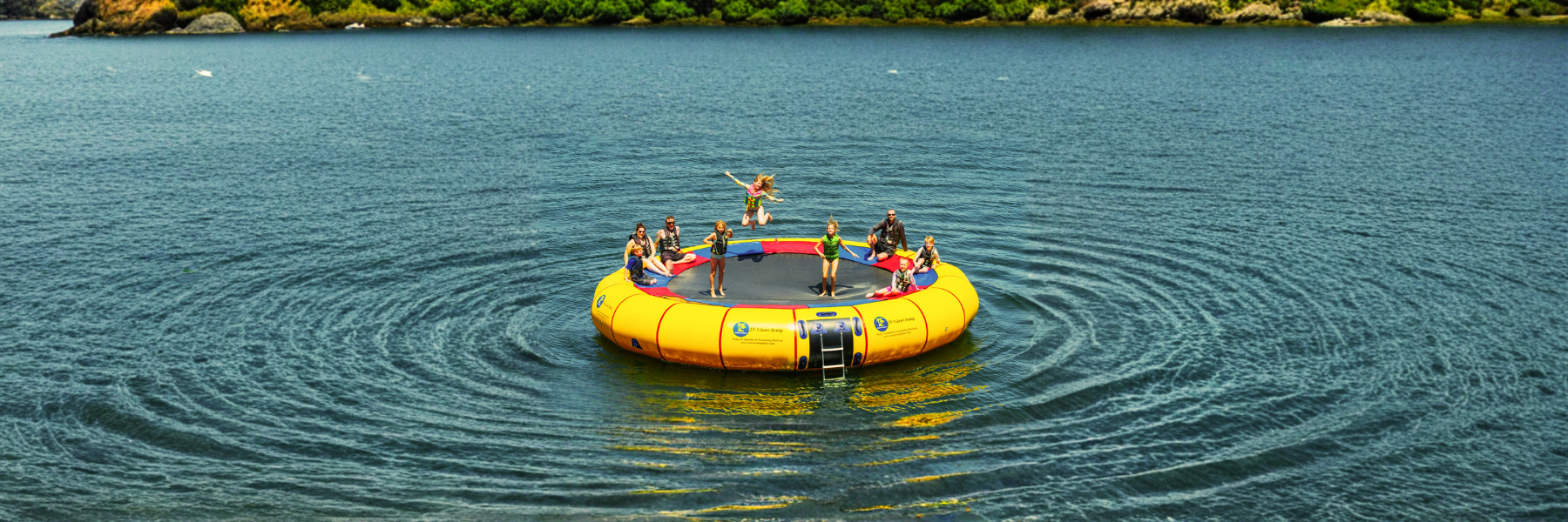 Yellow inflatable trampoline with people on a body of water - Water Trampoline vs Water Bouncer