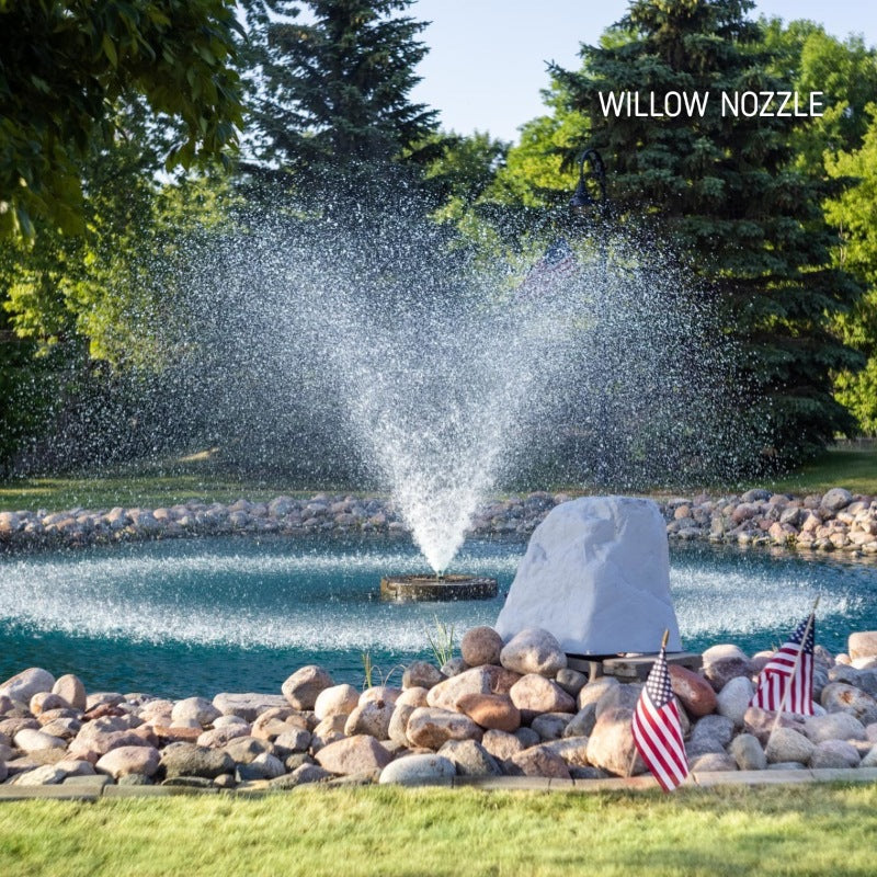 Kasco J Series Fountain with Willow Nozzle spray pattern in daytime decorative rock pond setting with American flags