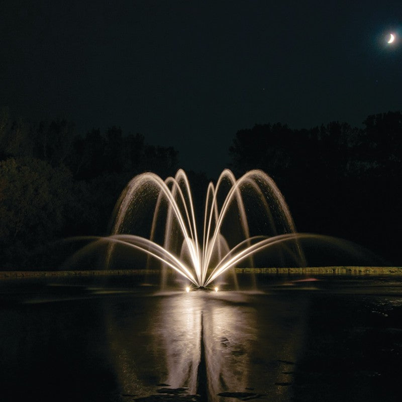 Kasco Magnolia Premium Fountain Nozzle - Fountain with illuminated water arches at night, surrounded by trees under a dark sky
