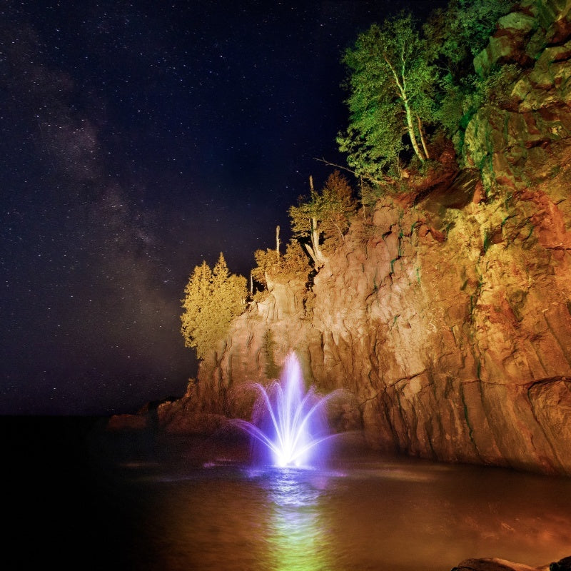 Kasco Mahogany Fountain Masterpiece Bundle illuminated at night with purple lighting near rocky cliff under starry sky