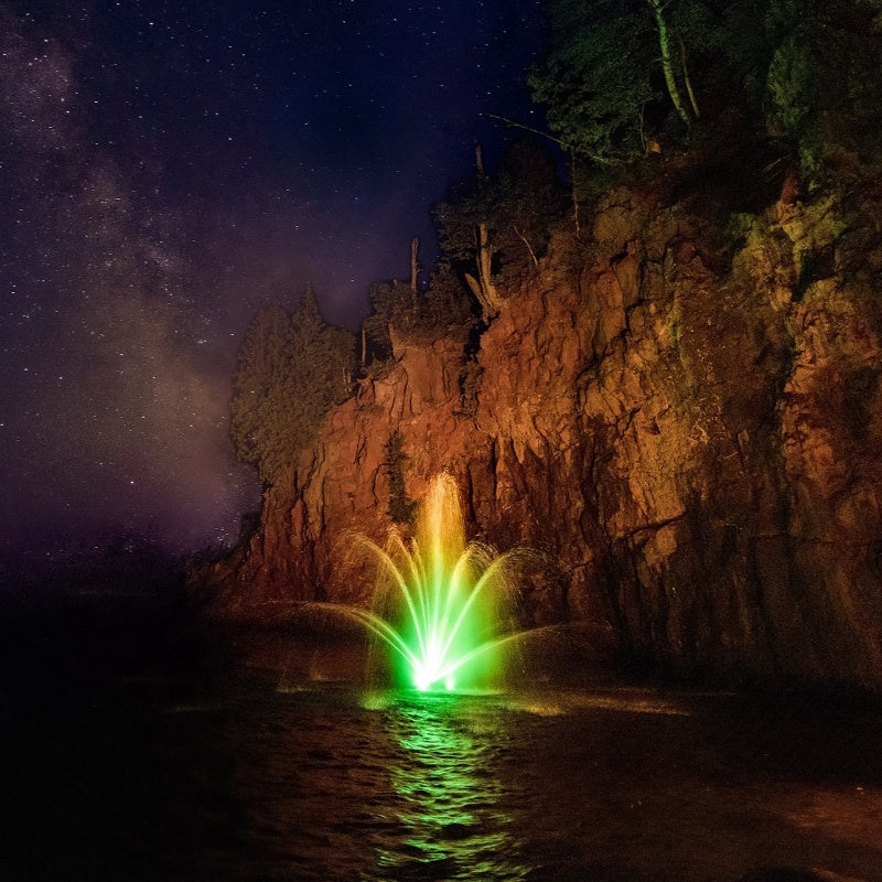 Kasco Mahogany Fountain illuminated at night with green lighting near rocky cliff under starry sky