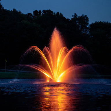Kasco Mahogany Fountain illuminated at night with orange lighting in golf course pond setting