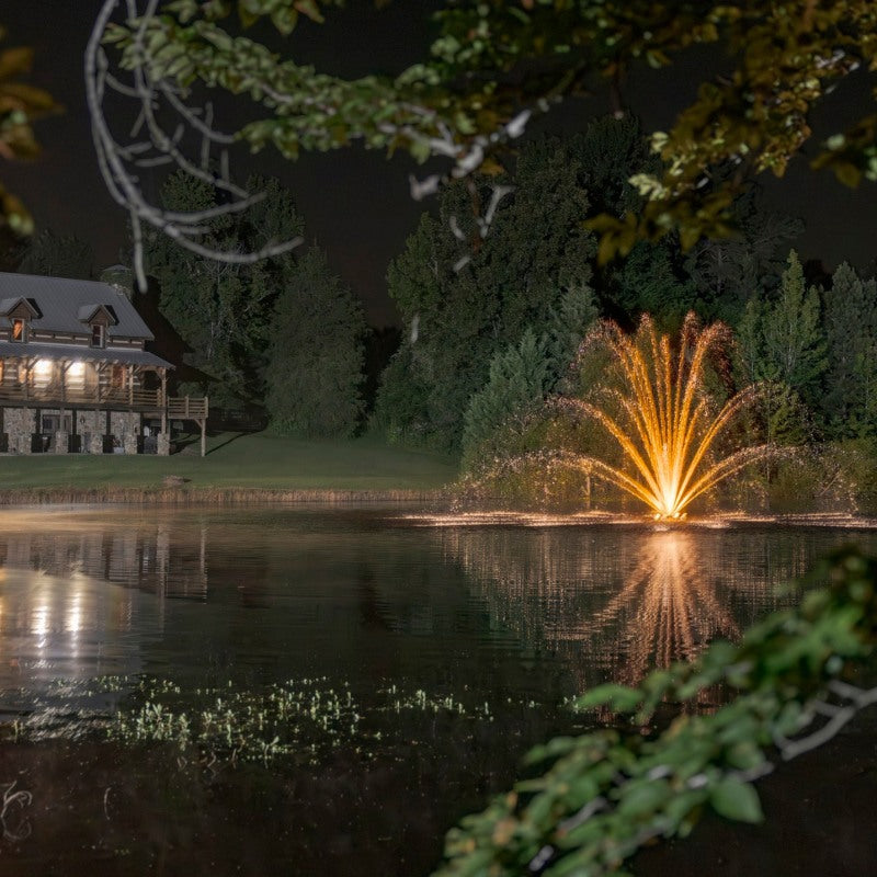 Kasco RGBW LED Lighting - RGBW18 LED Lighting System illuminating a pond fountain with warm white light near a lakeside home at night