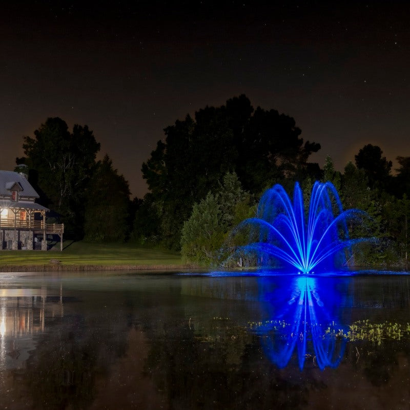 Kasco RGBW LED Lighting - RGBW18 LED Lighting System lighting a pond fountain in bright blue at night with reflections on the water