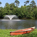 Kasco VFX Aerating Fountain producing a circular spray pattern on a lake with a canoe resting on the grassy shoreline