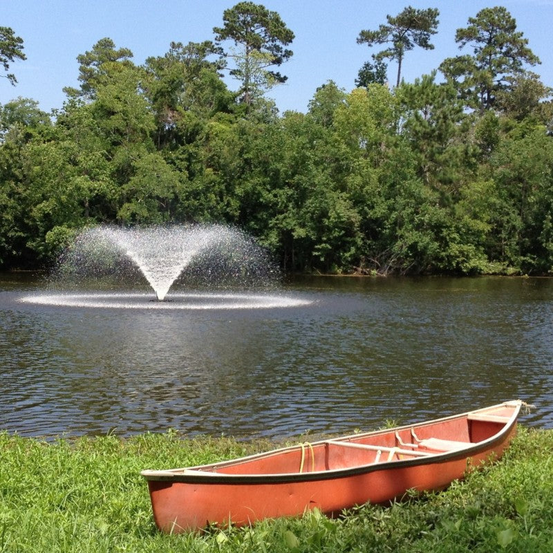 Kasco VFX Aerating Fountain producing a circular spray pattern on a lake with a canoe resting on the grassy shoreline