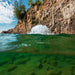 Kasco surface aerator churning water near rocky cliff shoreline with visible underwater clarity