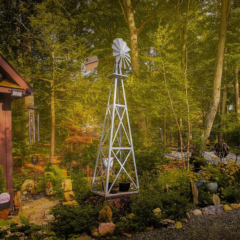 Outdoor Water Solutions Decorative Backyard Windmill installed among trees and landscaping in a residential yard