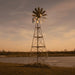Outdoor Water Solutions Super Premier 3-Leg Windmill Pond Aerator installed beside a pond on a rural property at sunset