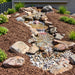 Savio Pond Free Waterfall Packages completed backyard pondless waterfall with natural rock edging, pebble streambed, mulch, and landscaping